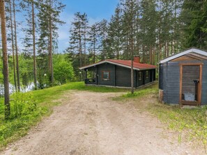 A cabin with a dirt path leading to it, surrounded by tall trees and a body of water.