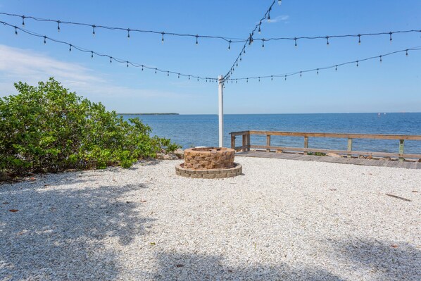 A gravel area with a stone fire pit, a wooden deck, and string lights.