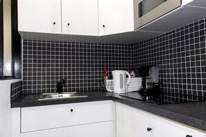 A kitchen with black and white tiles, a coffee maker, and a kettle. - Aboukir Design Flat 1 (Paris)