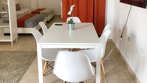 A modern living room with a white dining table, white chairs, a TV mounted on the wall, and a red curtain. - Boulevard Park IV 104 - This is Puerto Rico (Mayagüez Pueblo)