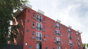 A red multi-story building with balconies, a gated entrance, and a parking lot. - Boulevard Park IV 104 - This is Puerto Rico (Mayagüez Pueblo)