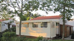 A covered caravan with a tiled roof, surrounded by greenery and a gravel path. - wooden chalet in the gardens of St Pierre (Saint-Pierre-D'oléron)