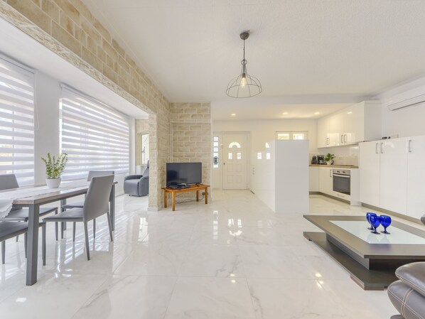 A modern living room with a TV, dining area, kitchen, and a stone wall.