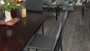 A modern living room with a sofa, a coffee table, and a dining table with chairs. There is a plant on the right side and a vase with flowers on the left.