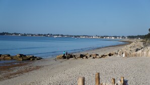 A sandy beach with a wooden fence in the foreground, a rocky shoreline, and a clear blue sky.