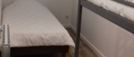 A small, single-room with a bunk bed, a window, and a radiator.