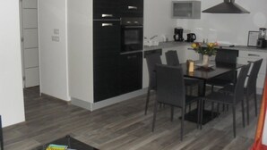A modern kitchen with black cabinets, a built-in oven, and a microwave. There is a dining table with chairs and a small side table with a vase of flowers.