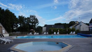 A rectangular swimming pool with a wooden deck surrounding it, equipped with lounge chairs and umbrellas.