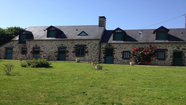 A stone building with multiple windows and doors, a grassy lawn in the foreground, and a clear blue sky.
