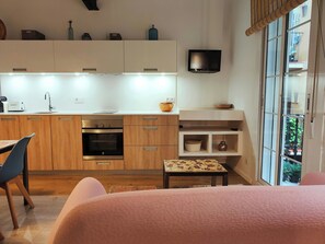 A modern kitchen with wooden cabinets, a built-in oven, a sink, and a flat-screen TV.
