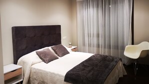 A neatly arranged hotel room with a large bed, a bedside table, a chair, and a window with sheer curtains. - Housing with sea views. (Sanxenxo)