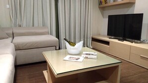 A modern living room with a sofa, a glass coffee table with a bottle and magazines, a TV on a stand, and a curtain in the background. - Housing with sea views. (Sanxenxo)