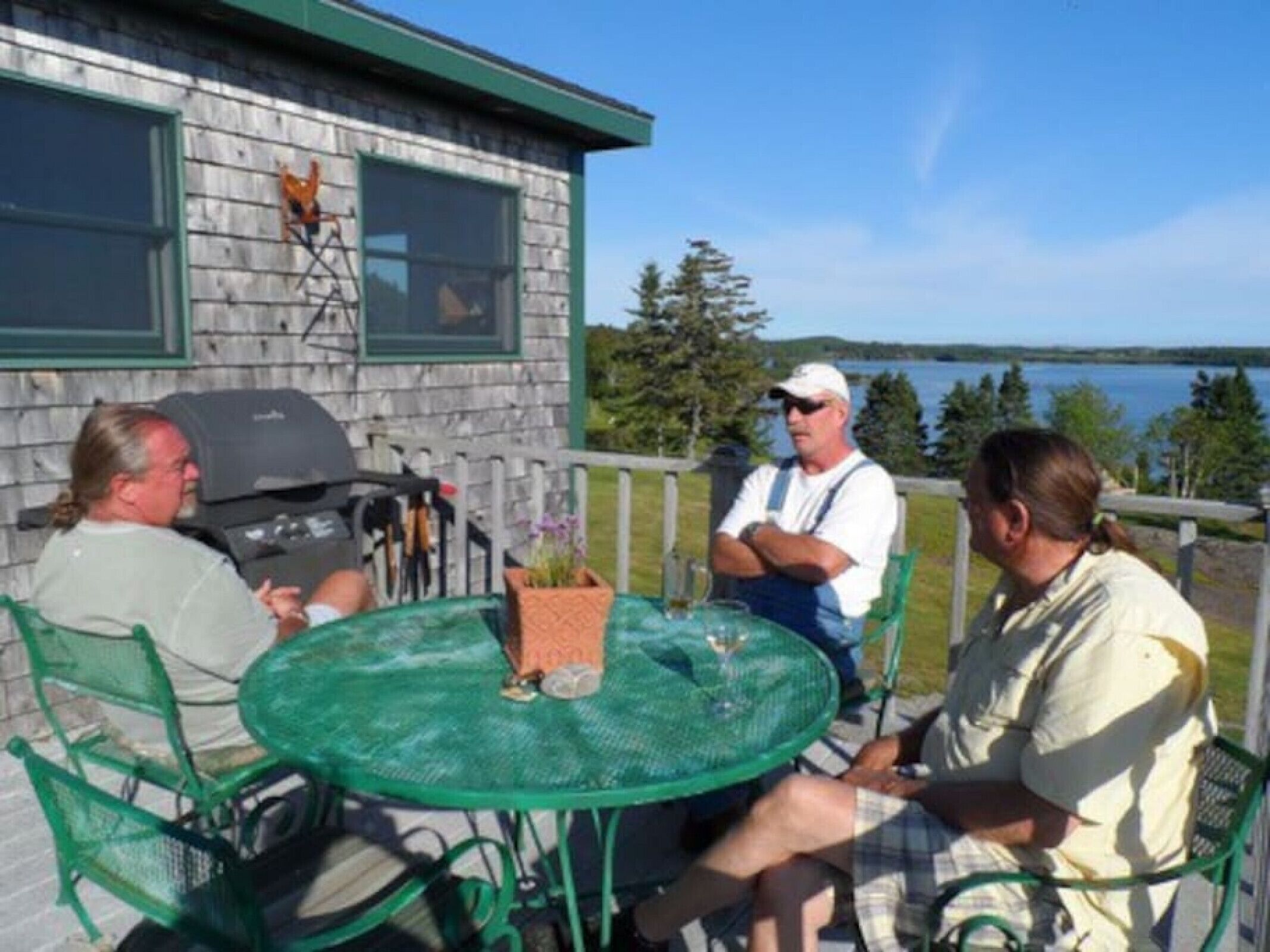 Une terrasse avec une table ronde et des chaises, un barbecue et une vue sur un lac.