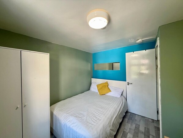 A bedroom with a bed, a wardrobe, a mirror, and a door.