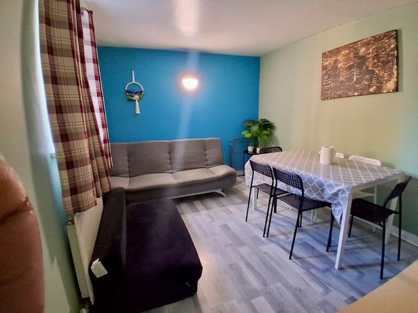 Una habitación con un sofá, una mesa de comedor con sillas, una pared azul y una planta.