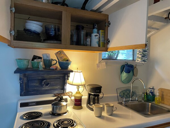 A kitchen with a stove, coffee maker, and a window above the sink. - Cozy Cottage Old Fashioned Charm (Rockport)