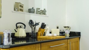 A kitchen with wooden cabinets, a black countertop, a kettle, a scale, and various utensils. - St John's Cottage - Simple2let Serviced Apartments (Halifax)