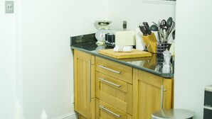 A kitchen with wooden cabinets, a black countertop, a stainless steel trash can, and a small table with candles. - St John's Cottage - Simple2let Serviced Apartments (Halifax)