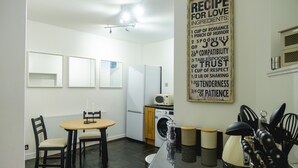 A compact kitchen with a dining area, a washing machine, and a wall-mounted recipe sign. - St John's Cottage - Simple2let Serviced Apartments (Halifax)