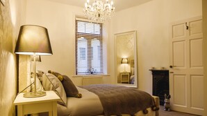 A bedroom with a bed, a bedside lamp, a window with blinds, a mirror, a fireplace, and a door. - St John's Cottage - Simple2let Serviced Apartments (Halifax)