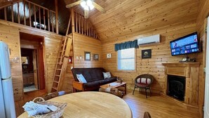 A cozy cabin interior with a wooden dining table, a sofa, a fireplace, and a television. - Ravine- Firepit, Pet Friendly, Cozy Cabin, WIFI, Pond, Gas Fireplace, off Blue Ridge Parkway (Laurel Springs)