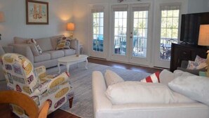A living room with a white sofa, a patterned armchair, a coffee table, and a ceiling fan. - Barefoot 'N Salty - Walk to Beach in Surfside Beach (Surfside Beach)