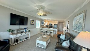 A living room with a TV, a ceiling fan, a dining area with chairs, a kitchen in the background, and a framed picture on the wall. - Surfwatch III 205 - Oceanfront Condominium in Surfside Beach (Surfside Beach)