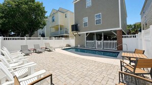 Un patio trasero residencial con piscina, sillas de deck blancas y un área de patio cubierta.