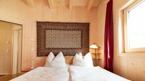 Ein Doppelbett mit floralem Bettzeug, eine gemusterte Wanddecke darüber, eine Nachttischlampe und ein Fenster mit roten Vorhängen.