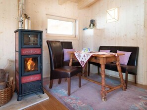 Ein gemütlicher Raum mit Kaminofen, zwei Ledersofas, einem Holztisch mit Tischdecke und einem Fenster.