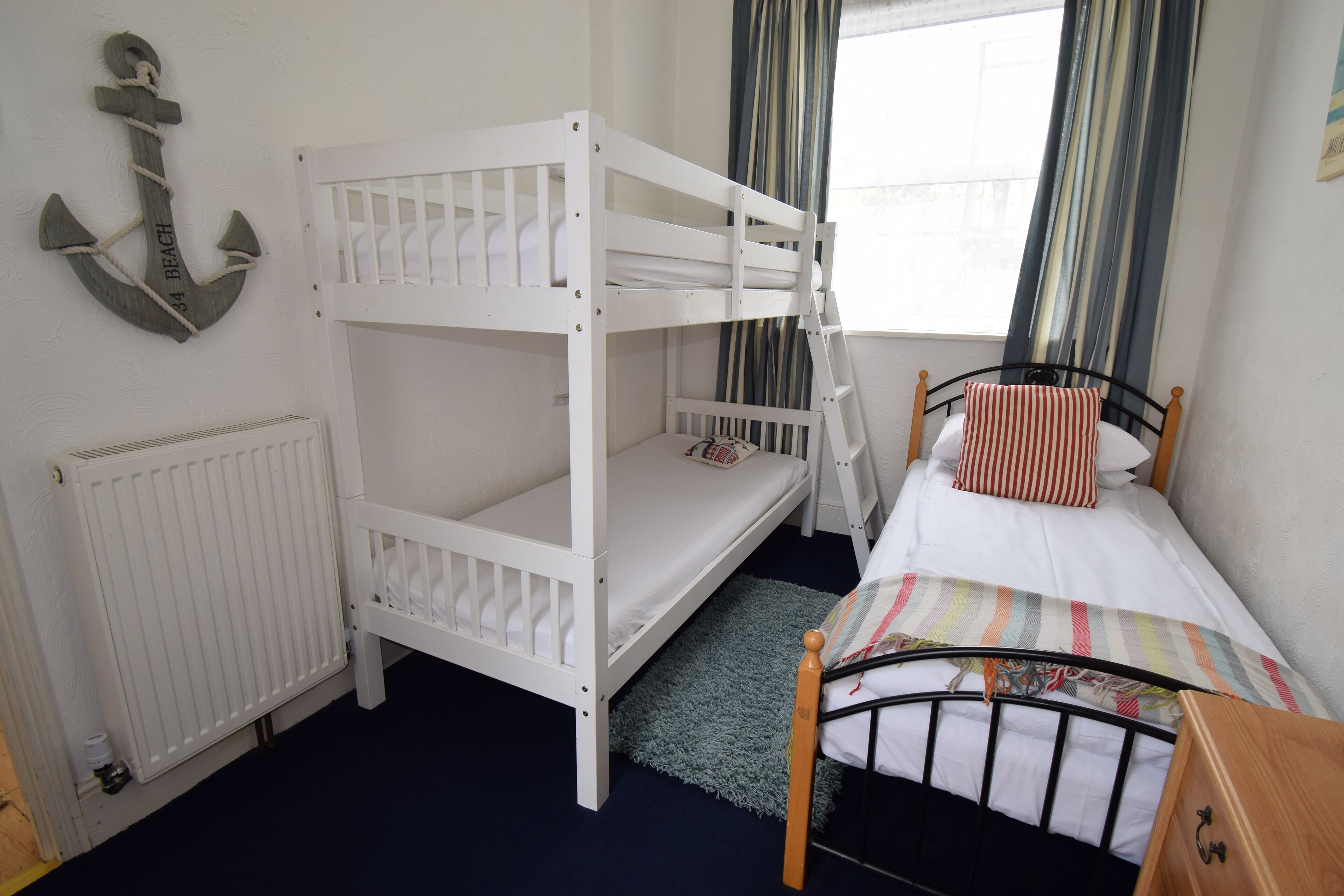 A bunk bed room with a white anchor decoration, a window with striped curtains, and a radiator.