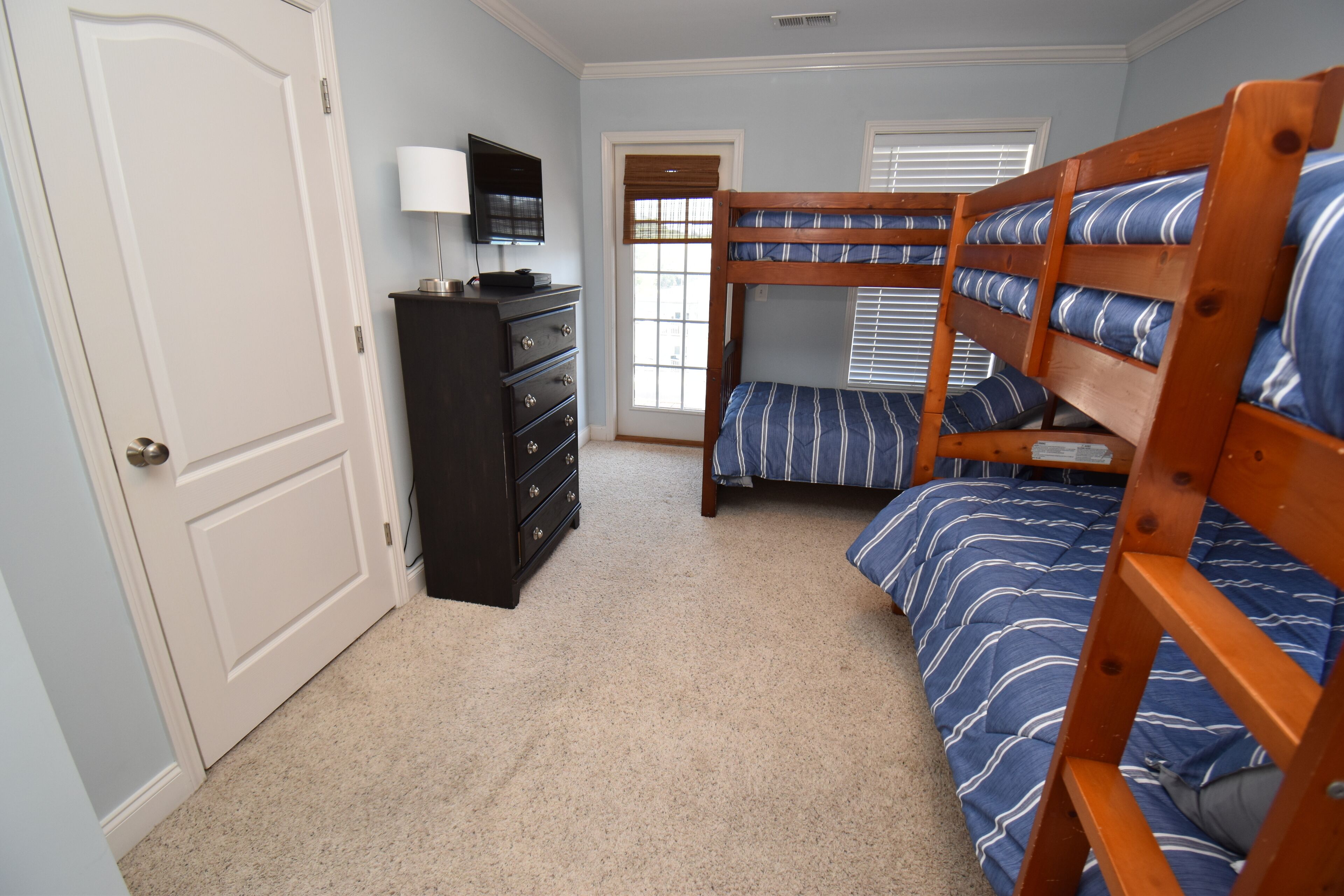 A bedroom with bunk beds, a dresser, a television, and a window with blinds.