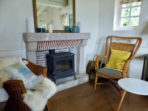 A room with a fireplace, wicker furniture, a round table, and a window with a view.
