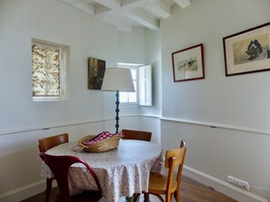 A dining area with a round table, chairs, a lamp, and framed artwork on the walls.