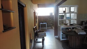 A kitchen with a stone wall, a wooden chair, a white cabinet, and a tiled floor. - Hostal Casa De Piedra (Humahuaca)