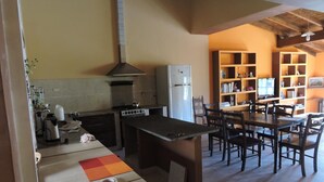 A compact kitchen with a stove, refrigerator, and a dining area with a table and chairs. - Hostal Casa De Piedra (Humahuaca)
