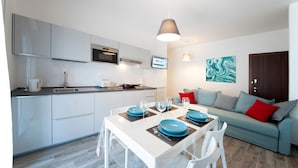 Una cocina moderna con armarios blancos, una zona de comedor con platos azules y un sofá gris con cojines rojos.