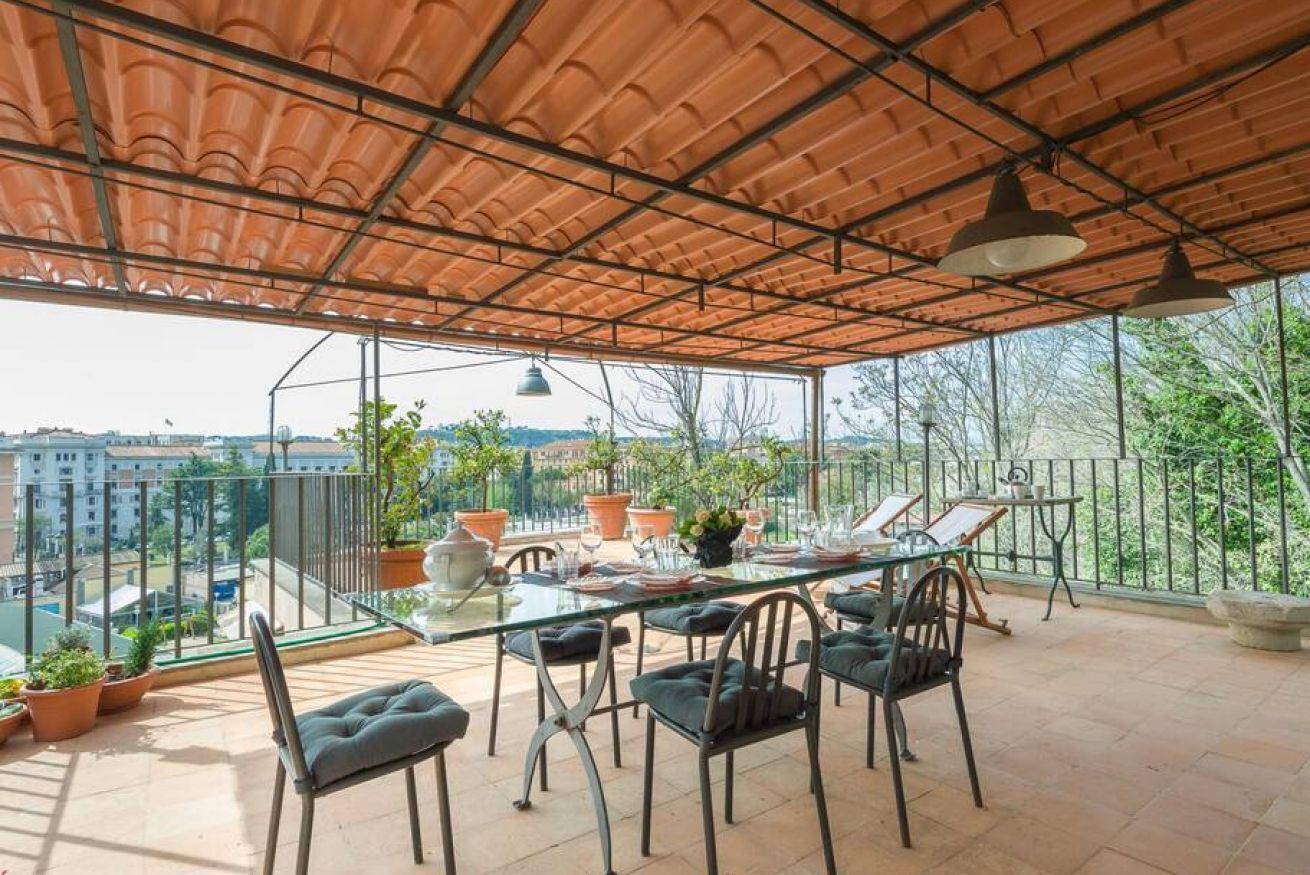 A terrace with a table set for dining, chairs, potted plants, and a view of the cityscape.