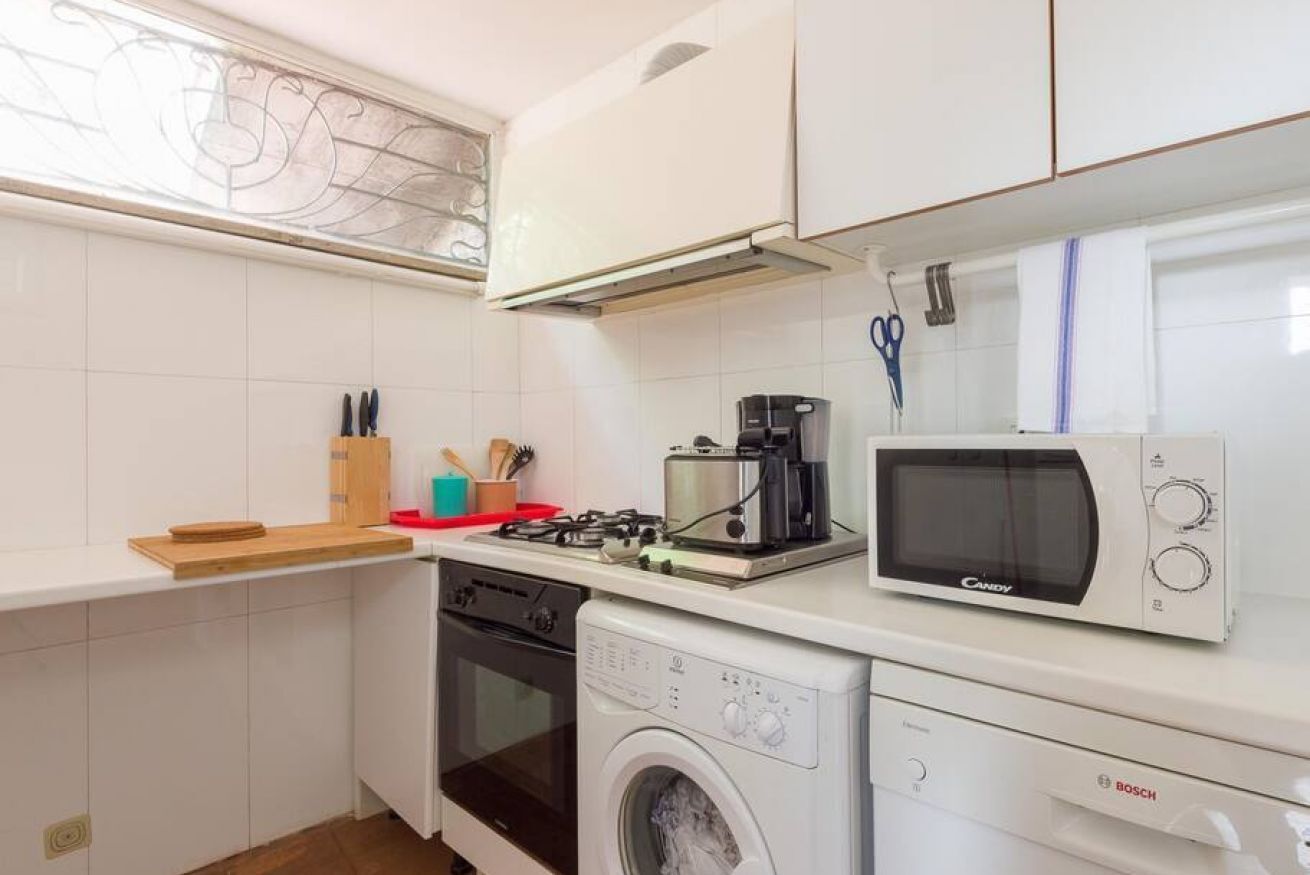 A compact kitchen with white cabinets, a Bosch washing machine, a microwave, and a gas stove.