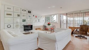 Un salon avec un canapé blanc, un téléviseur, une table à manger avec des chaises et un mur décoré de tableaux encadrés.