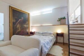 Quarto com cama, sofá, quadro, luminárias de cabeceira e escada.