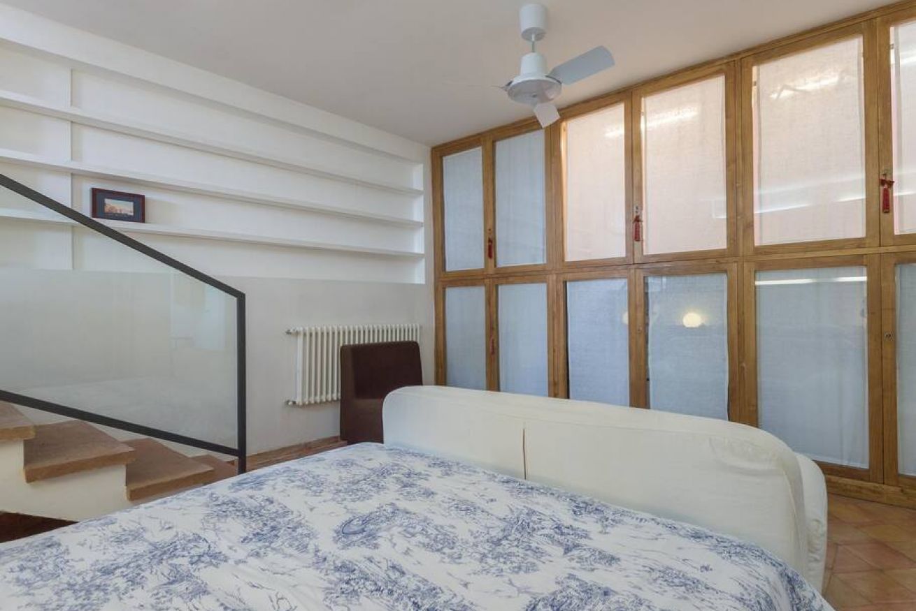 A bedroom with a bed, a window with blinds, a radiator, and a ceiling fan.