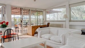 Un salon moderne avec un canapé blanc, une table à manger avec des chaises et une grande fenêtre donnant sur la forêt.