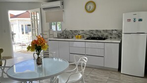 Una cocina moderna con armarios blancos, un refrigerador blanco, una mesa de vidrio con sillas y un reloj amarillo en la pared.