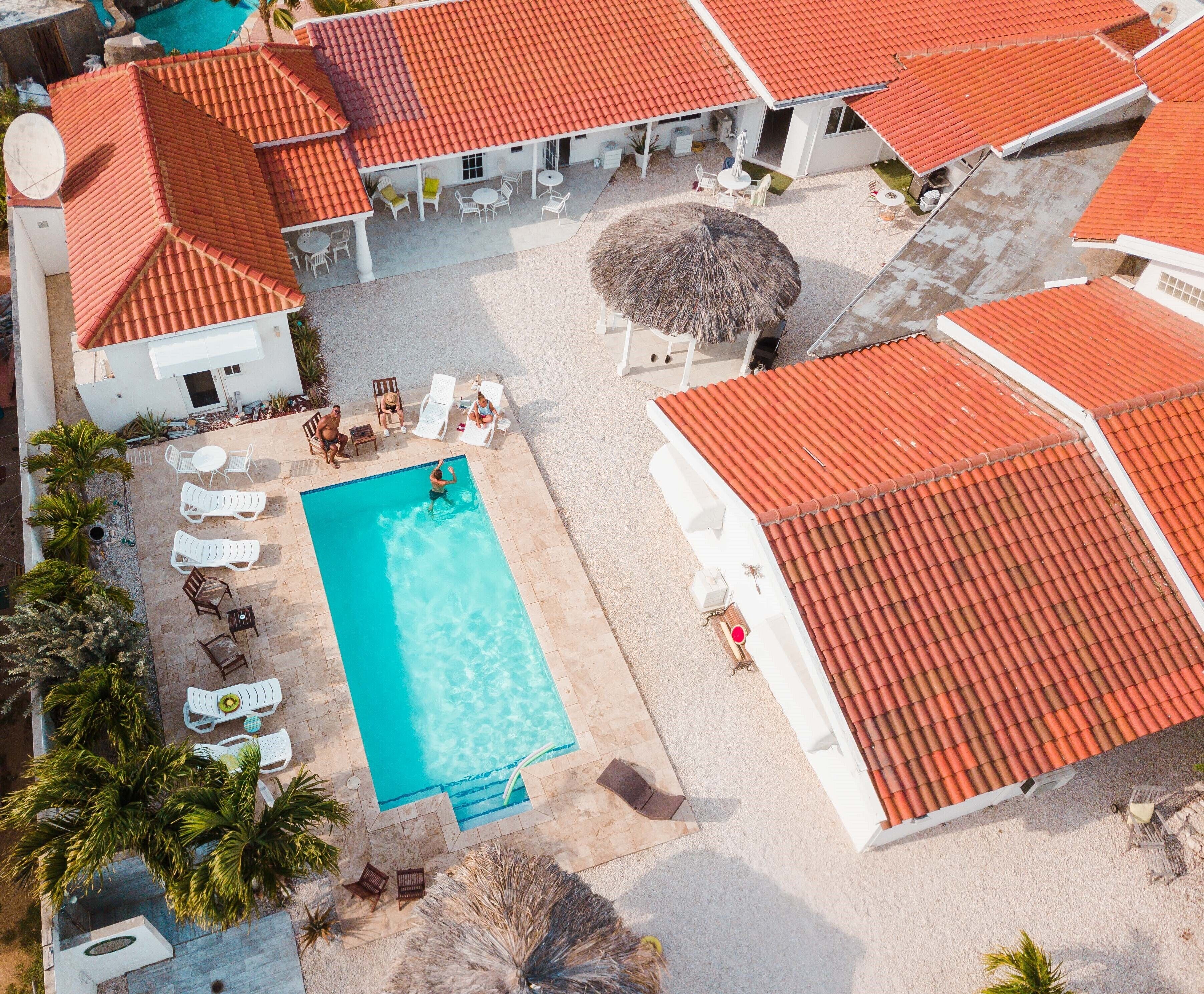 An aerial view of a resort with a swimming pool, lounge chairs, and a thatched umbrella.