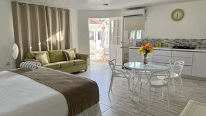 Habitación de hotel con cama, sofá, mesa de comedor con sillas, zona de cocina y vistas al exterior.