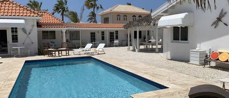 A swimming pool with lounge chairs, a pergola, and a small table with a bottle and glasses.