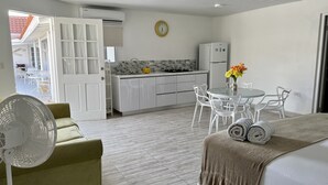 Una cocina moderna con armarios blancos, un comedor con sillas blancas y un ventilador en primer plano.