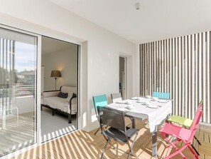 A modern room with a glass door leading to a balcony, a dining table set with white tableware, and a sofa with pillows.