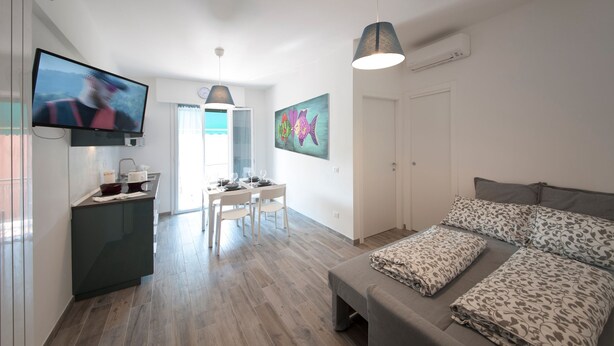 Una sala moderna con televisión de pantalla plana, comedor con mesa y sillas, y cama con ropa de cama estampada.